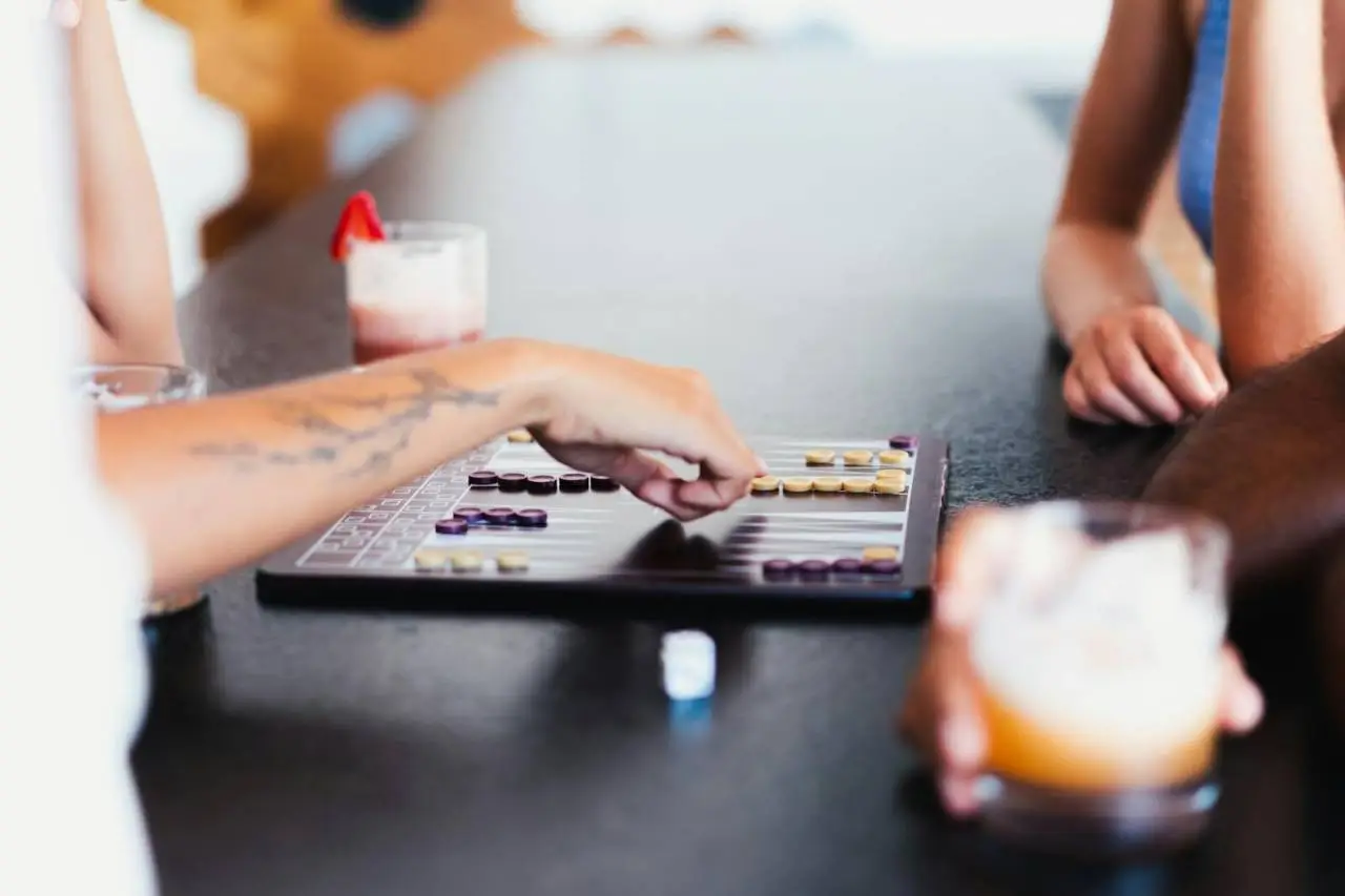 A detailed close-up of friends enjoying a board game and cocktails at a bar counter, creating a lively and social atmosphere.