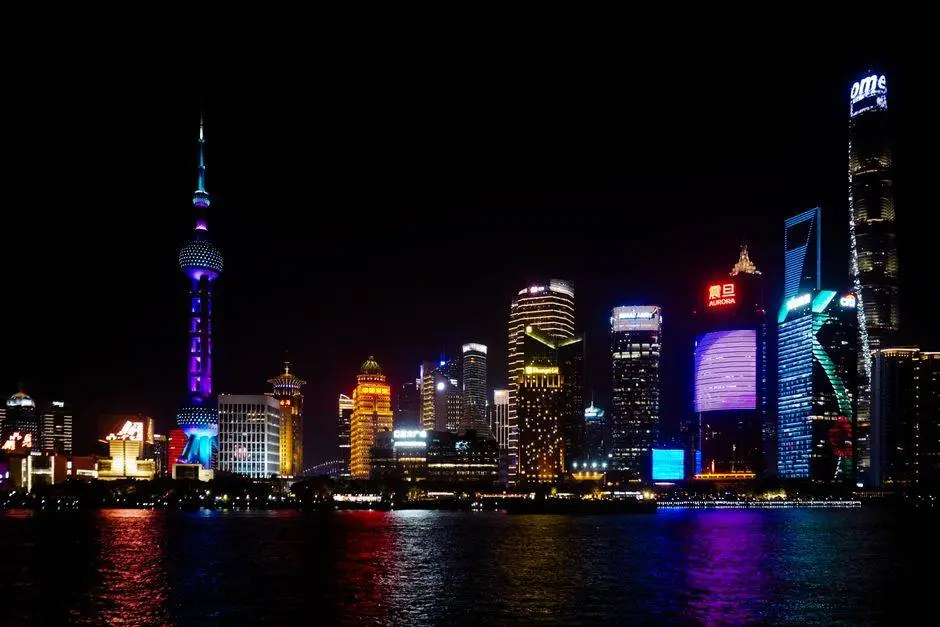 Vibrant Shanghai skyline at night featuring iconic skyscrapers and colorful lighting reflections on water.