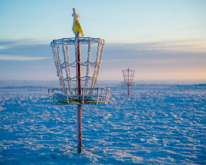 Frosty disc golf basket in a snowy open field during a winter sunrise, capturing serene outdoor vibes.