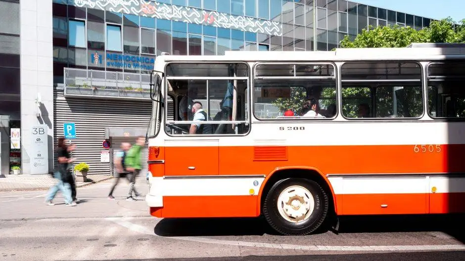 A classic red and white bus travels through Bratislava's urban landscape with pedestrians nearby.