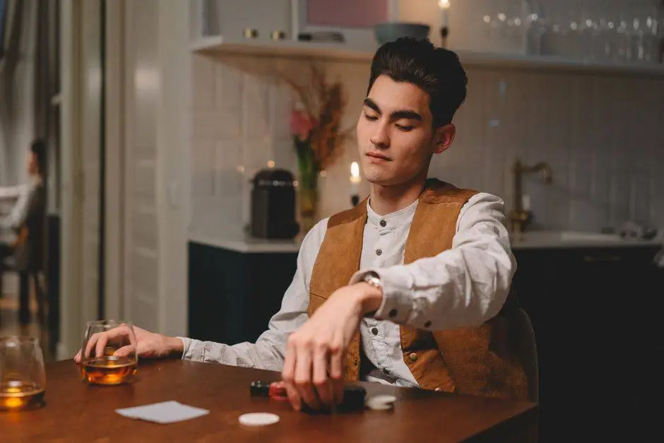 A man sits at a wooden table playing poker indoors, contemplating his next move.
