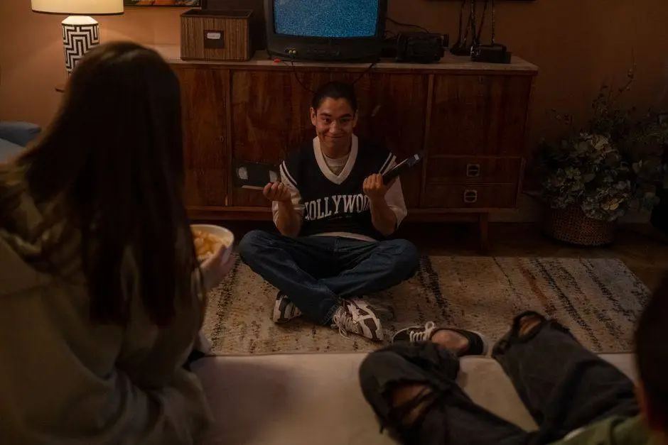 A group of teenagers enjoy a nostalgic movie night at home with VHS tapes and snacks.